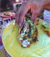 My hands holding a pork belly taco from a street stall in Mexico City.